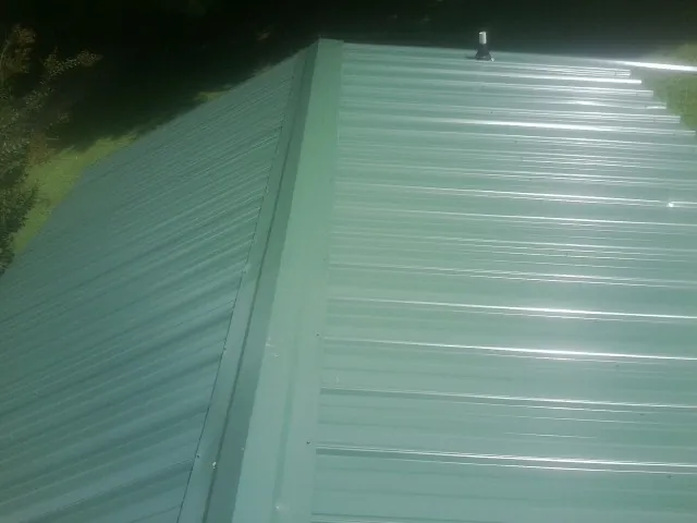New green metal panels meeting at the ridge of a roof — Flat Roof Repair work by our crew in Walnut Grove
