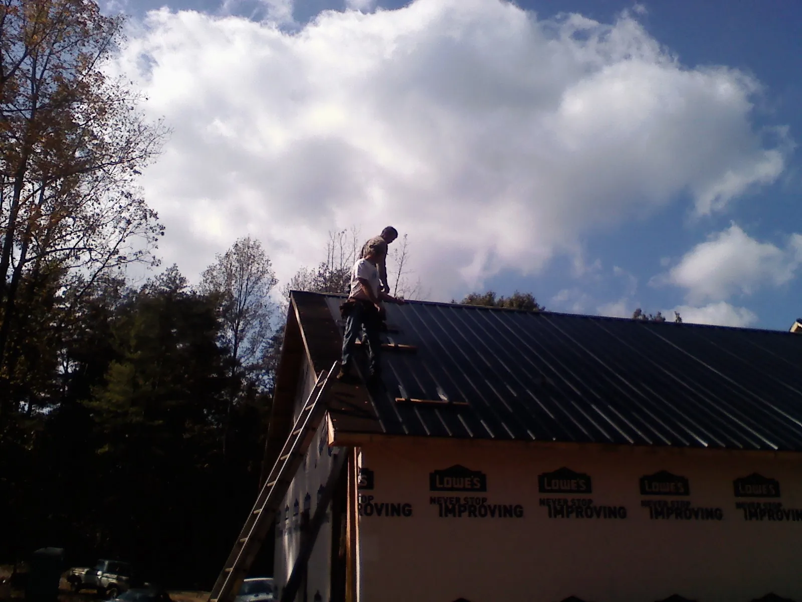 Roofer fastening dark metal panels high against a cloudy sky, from a Roof Inspection job in Walnut Grove